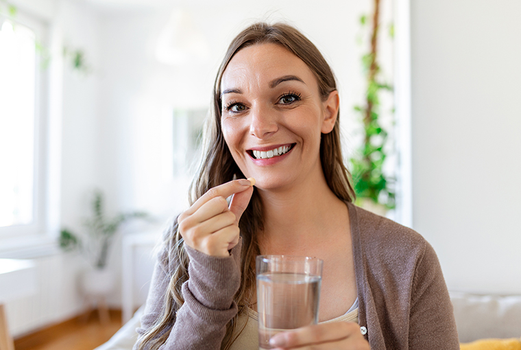 Eine Frau nimmt B12 Ankermann als Tablette mit Wasser zu sich.